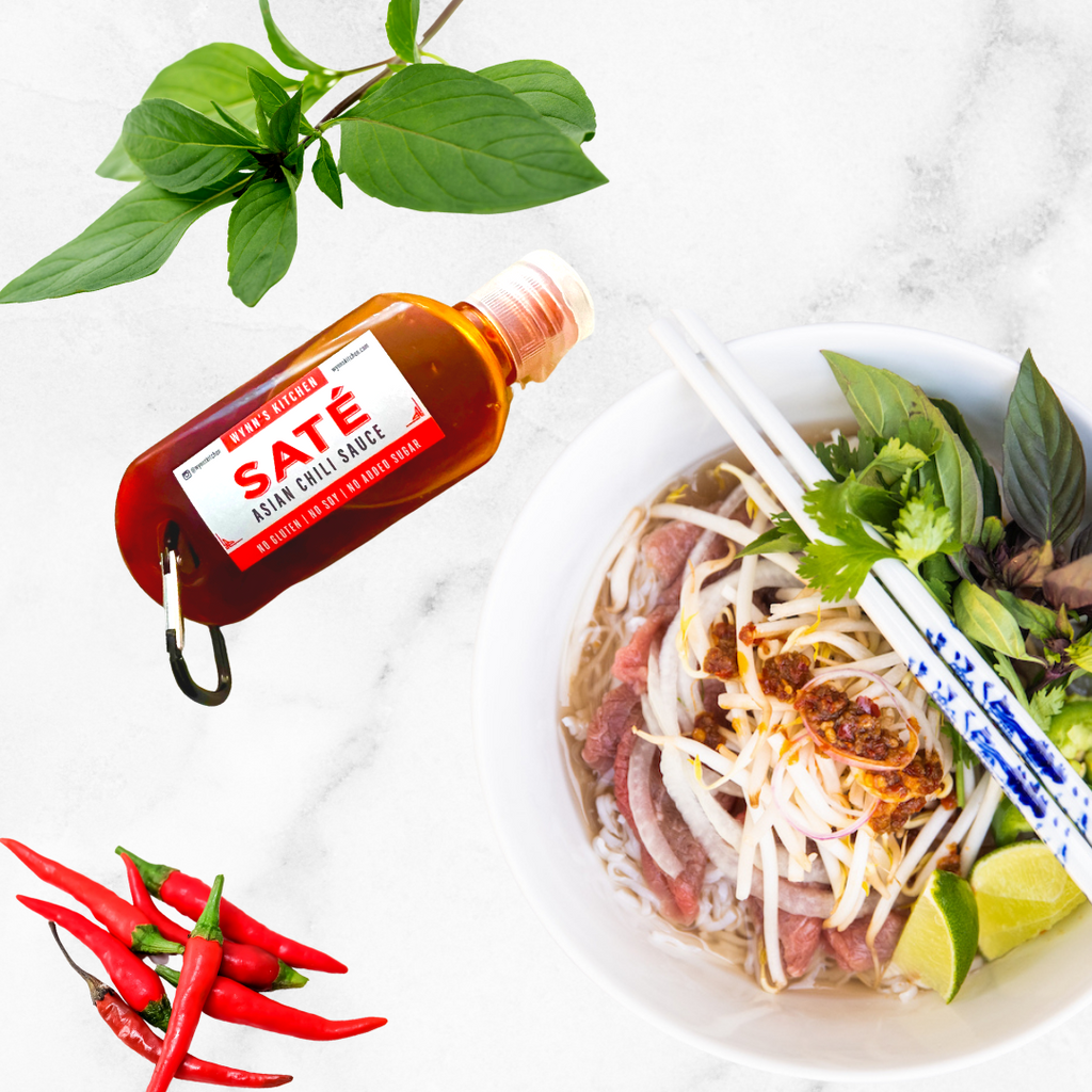 A white bowl filled with noodles, meat and vegetables next to a keychain bottle of sauce.